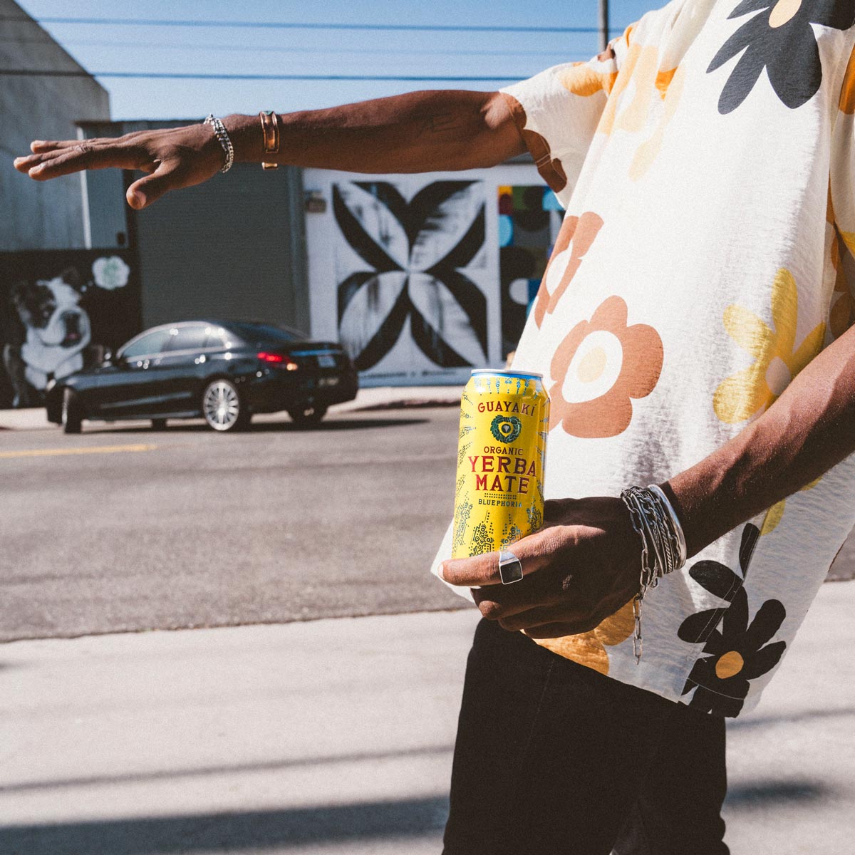 A person holding up a Yerba Mate can. In the backfround there is a car.
