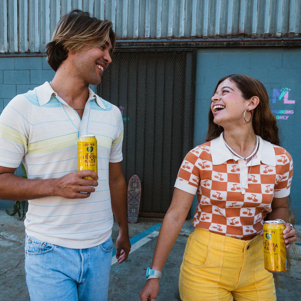2 people smiling and walking holding Guayaki Yerba Mate cans.