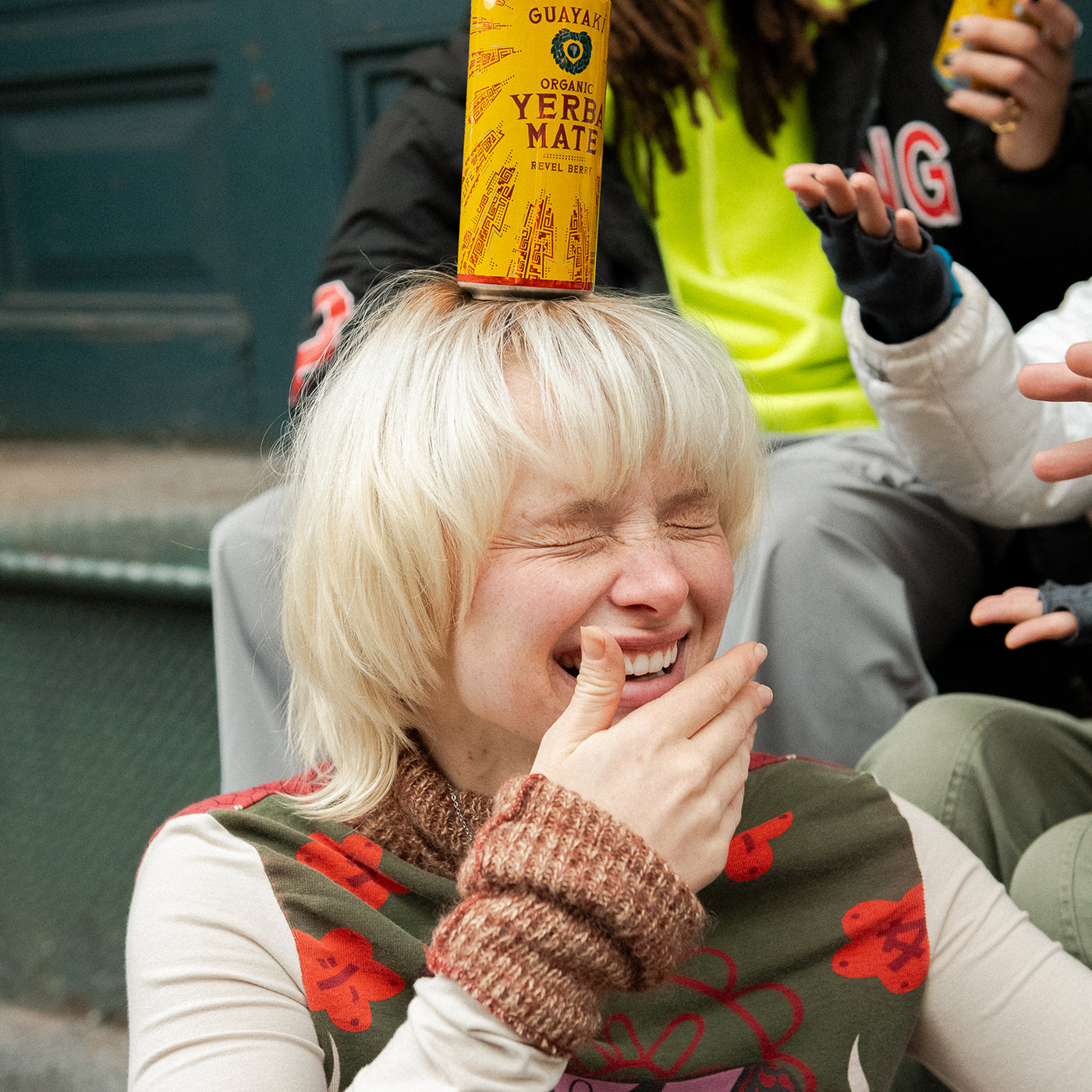 Young person smiles with a can of Yerba Madre balanced on their head