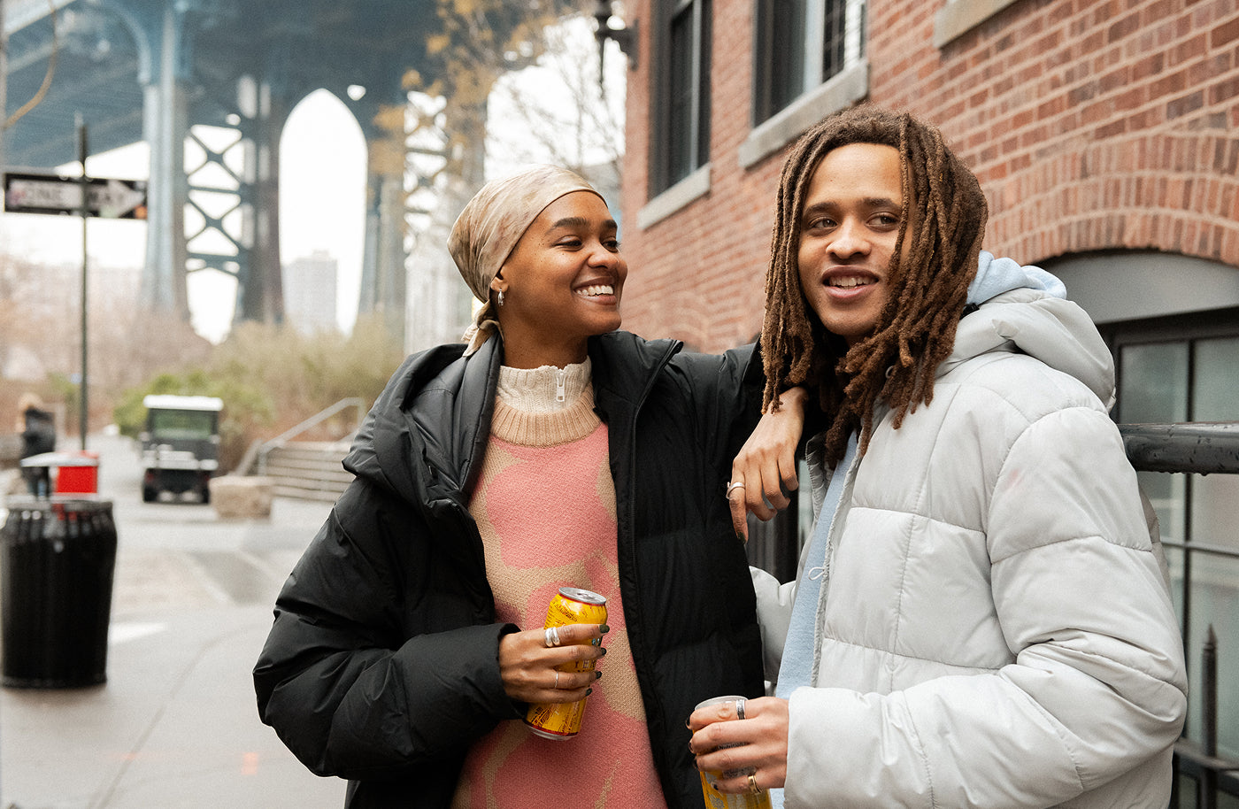 Two young people stand happily in downtown Brooklyn, holding cans of Yerba Madre.